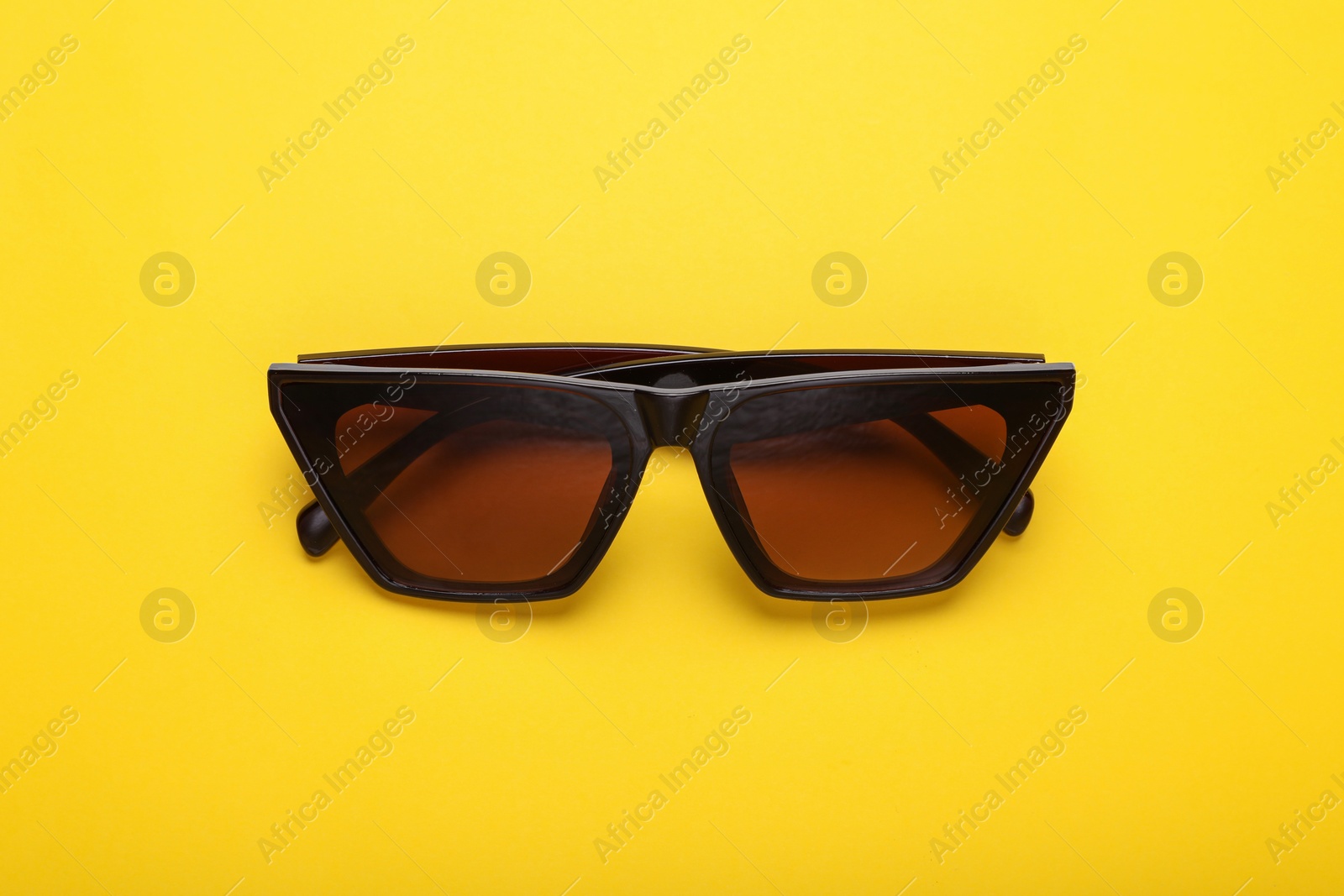 Photo of Stylish sunglasses on yellow background, top view