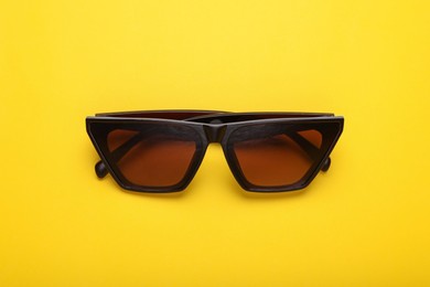 Photo of Stylish sunglasses on yellow background, top view