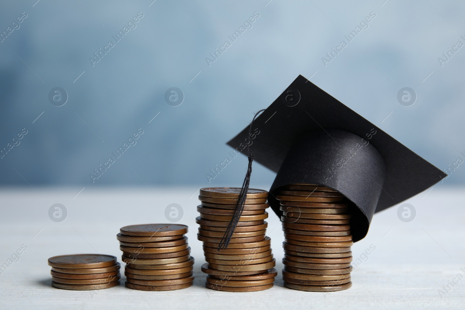 Photo of Coins and student graduation hat on white wooden table against blue background. Tuition fees concept