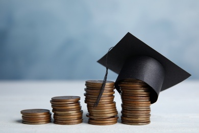 Photo of Coins and student graduation hat on white wooden table against blue background. Tuition fees concept