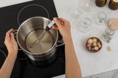 Photo of Woman measuring temperature of melted wax in kitchen, closeup. Making homemade candles