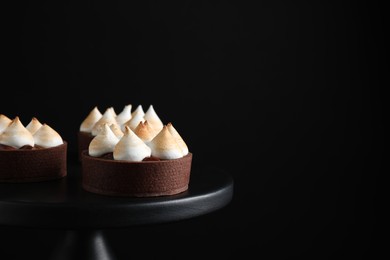 Photo of Delicious salted caramel chocolate tarts on stand against dark background, closeup. Space for text
