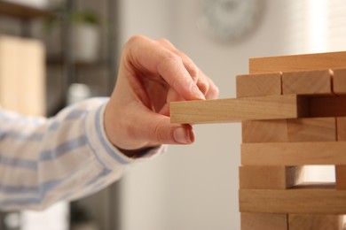 Photo of Playing Jenga. Woman removing wooden block from tower indoors, closeup