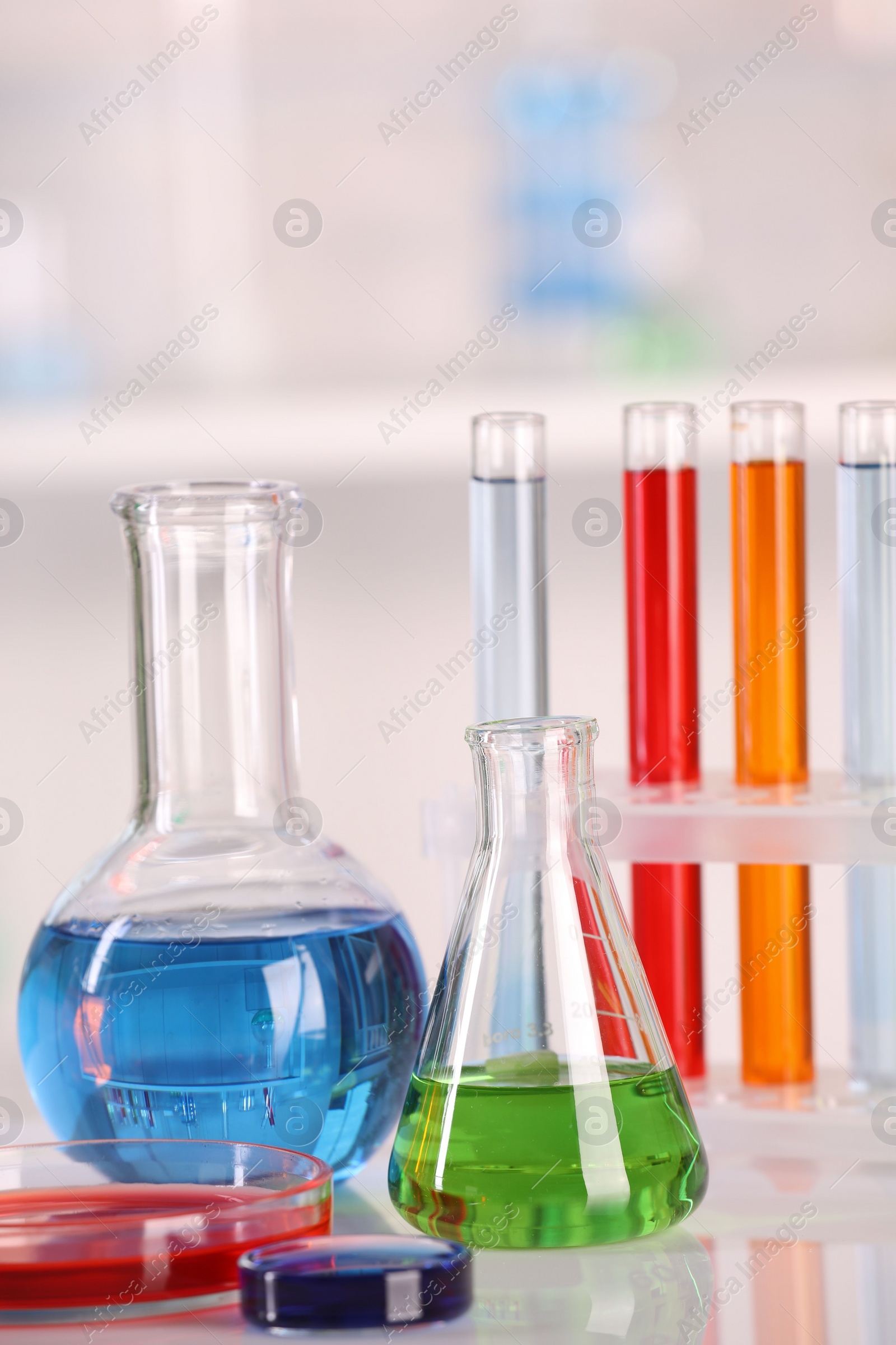 Photo of Laboratory analysis. Glass flasks, Petri dish and test tubes with liquids on white table against blurred background