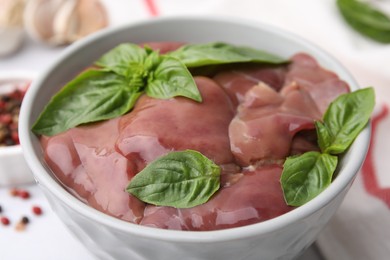 Photo of Bowl with raw chicken liver and basil on table, closeup