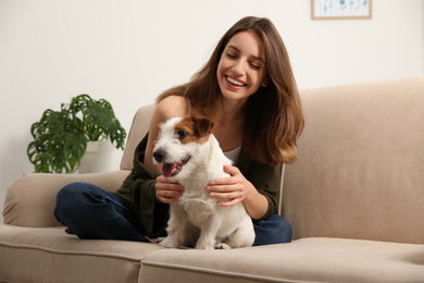 Photo of Young woman with her cute Jack Russell Terrier on sofa at home. Lovely pet