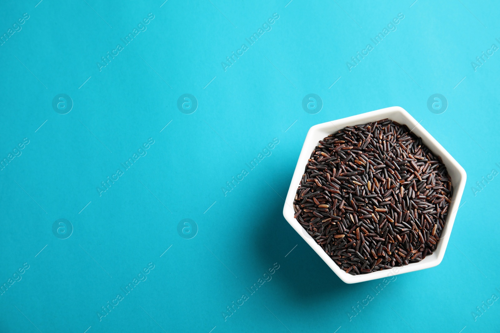 Photo of Bowl with uncooked black rice on color background, top view. Space for text