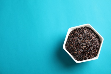 Bowl with uncooked black rice on color background, top view. Space for text