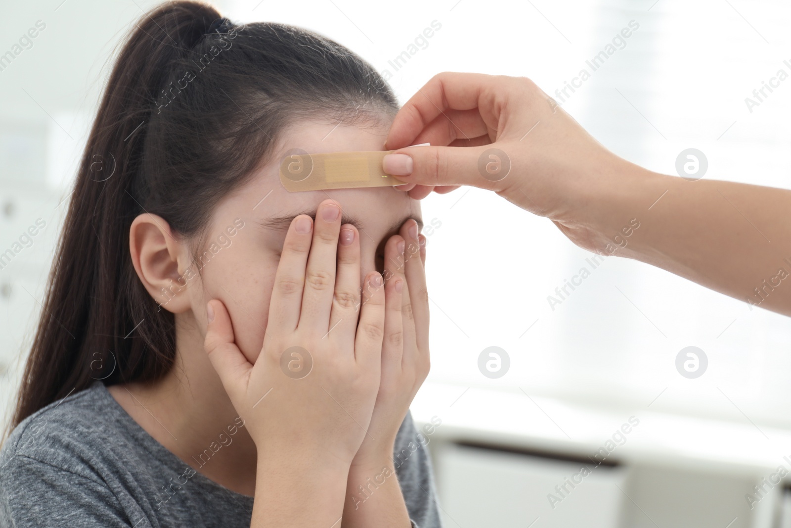 Photo of Mother putting sticking plaster onto daughter's forehead indoors