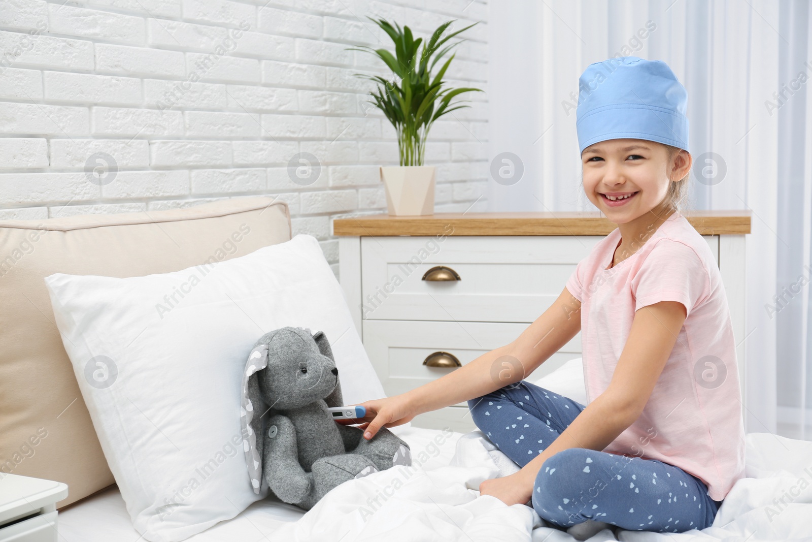 Photo of Cute child playing doctor with stuffed toy on bed in hospital ward