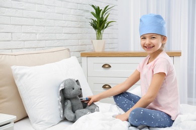 Cute child playing doctor with stuffed toy on bed in hospital ward