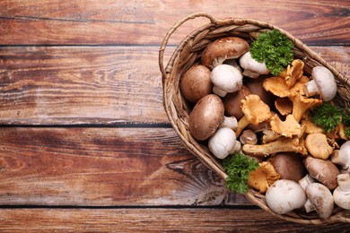 Photo of Basket with different mushrooms on wooden table, top view. Space for text