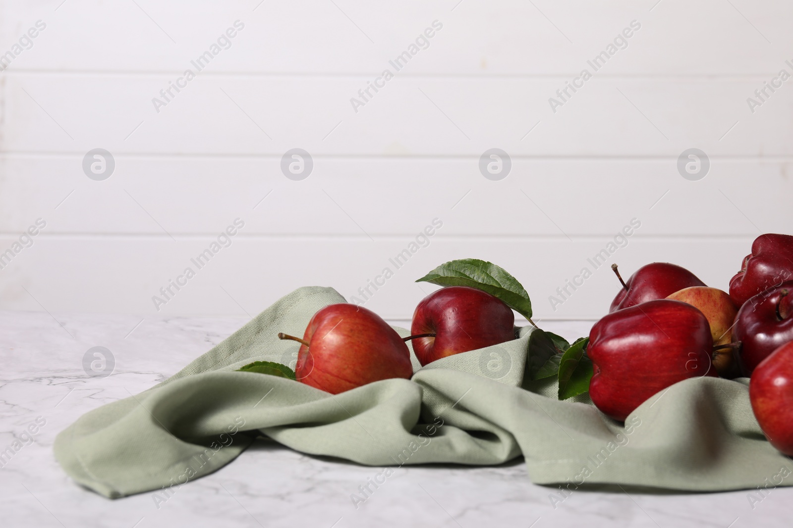 Photo of Fresh ripe red apples with leaves on white marble table. Space for text