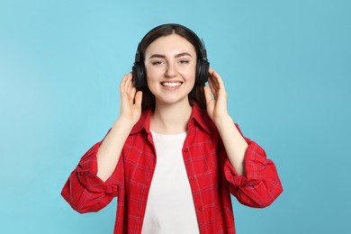 Photo of Happy woman in headphones enjoying music on light blue background
