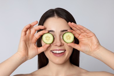 Woman holding pieces of cucumber on light grey background. Spa treatment