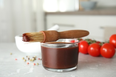 Photo of Glass bowl of barbecue sauce with basting brush on table