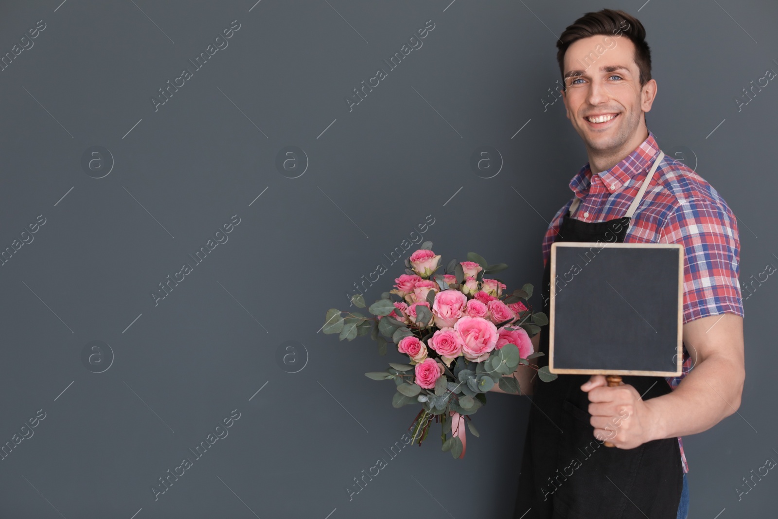 Photo of Male florist holding small chalkboard and bouquet on dark background