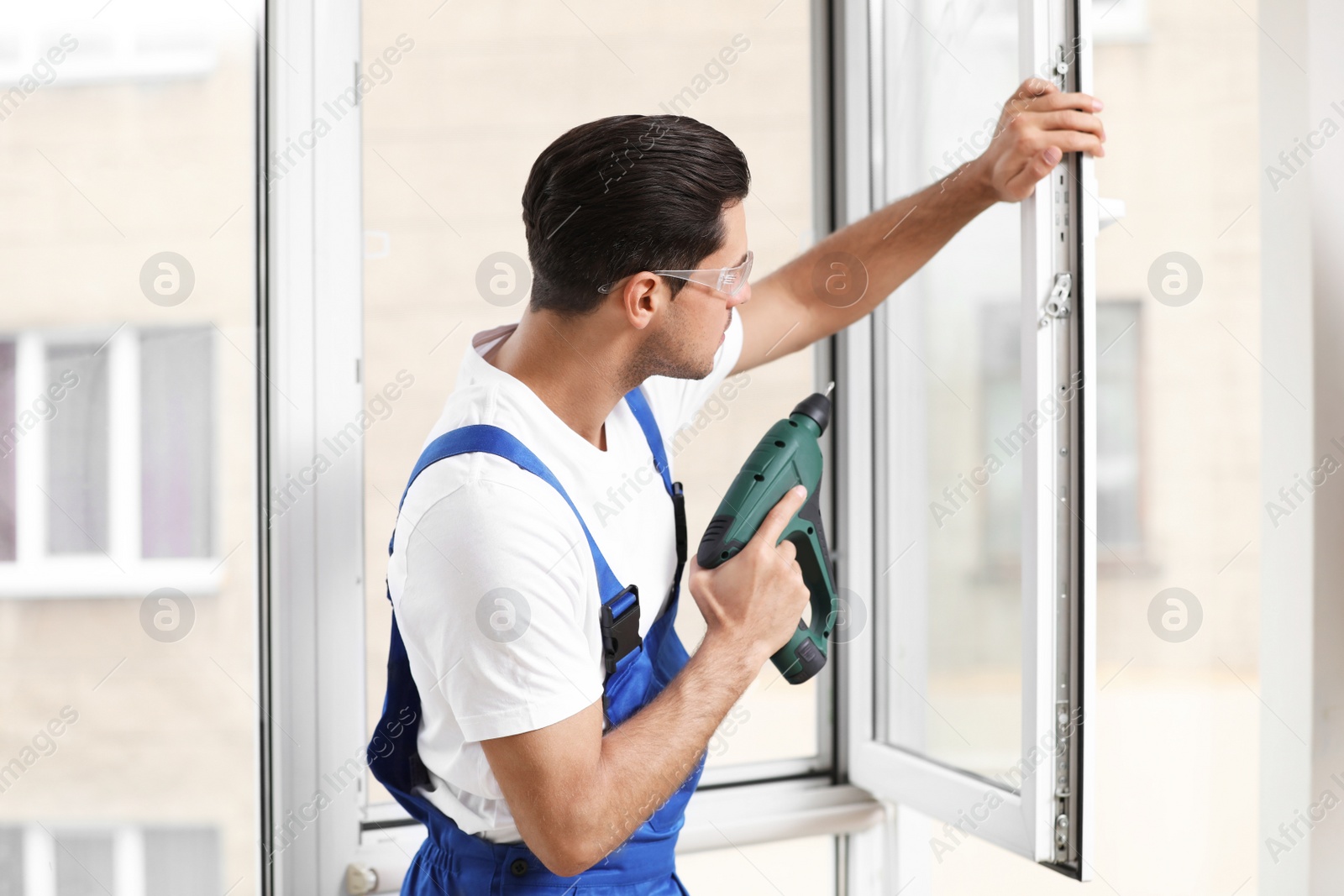 Photo of Construction worker repairing plastic window with electric screwdriver indoors