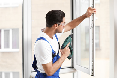 Photo of Construction worker repairing plastic window with electric screwdriver indoors