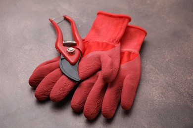 Photo of Pair of red gardening gloves and secateurs on brown textured table