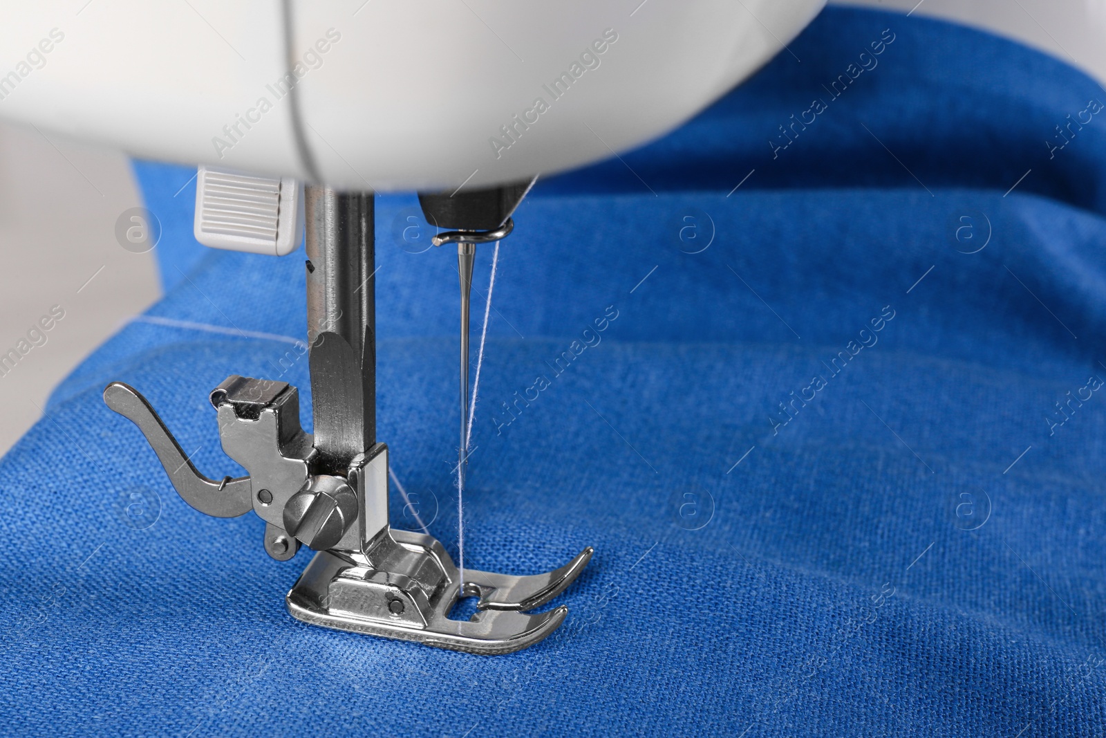 Photo of Modern sewing machine with blue cloth, closeup