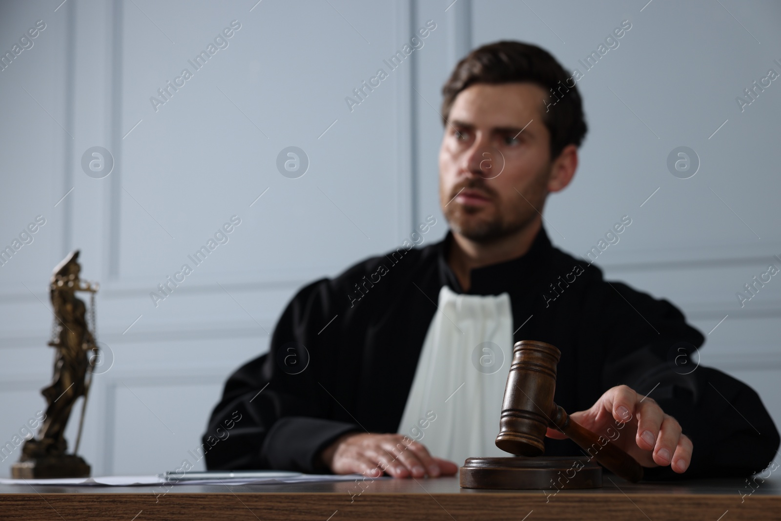 Photo of Judge with gavel sitting at wooden table indoors, selective focus