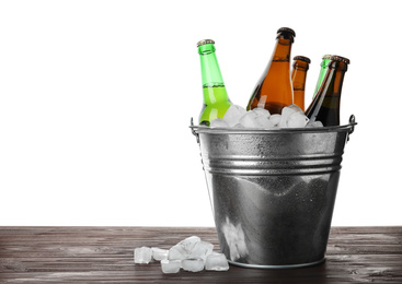 Photo of Metal bucket with bottles of beer and ice cubes on wooden table against white background. Space for text