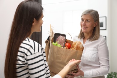 Photo of Courier giving paper bag with food products to senior woman indoors