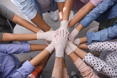 People in white medical gloves stacking hands indoors, top view