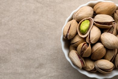Photo of Bowl with pistachio nuts on beige tablecloth, top view. Space for text