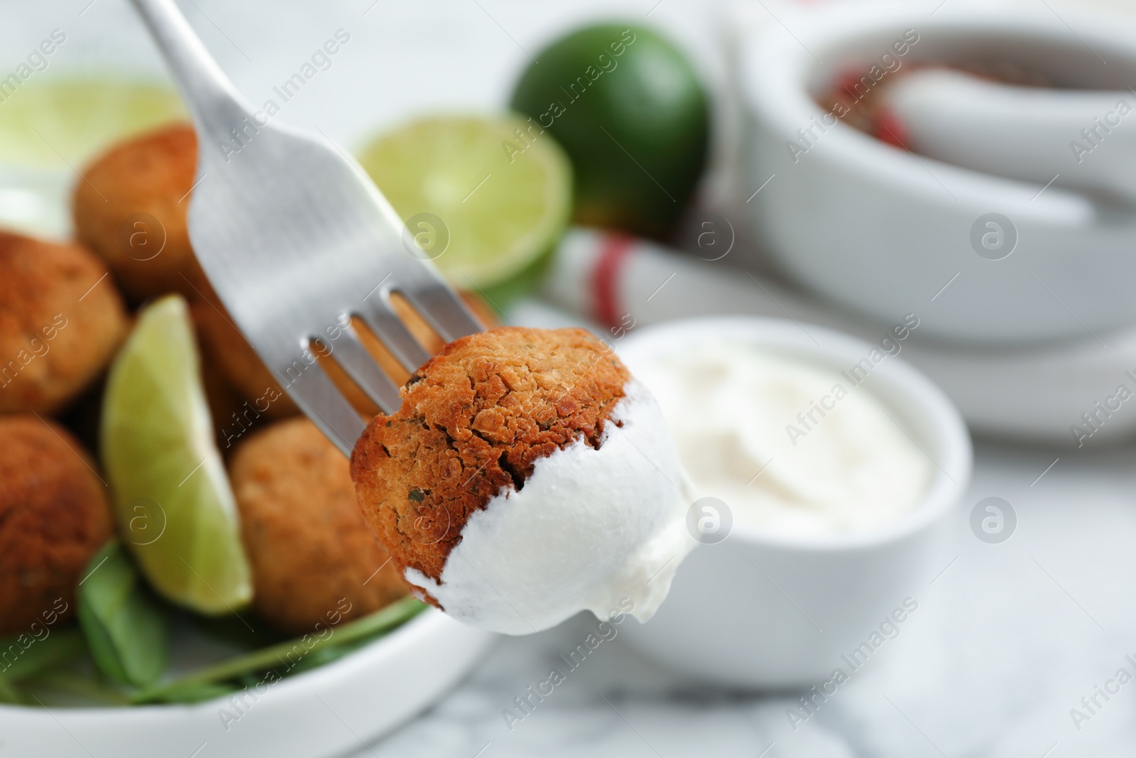 Photo of Fork with delicious falafel ball and sauce over table, closeup