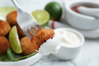 Photo of Fork with delicious falafel ball and sauce over table, closeup
