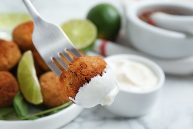 Fork with delicious falafel ball and sauce over table, closeup