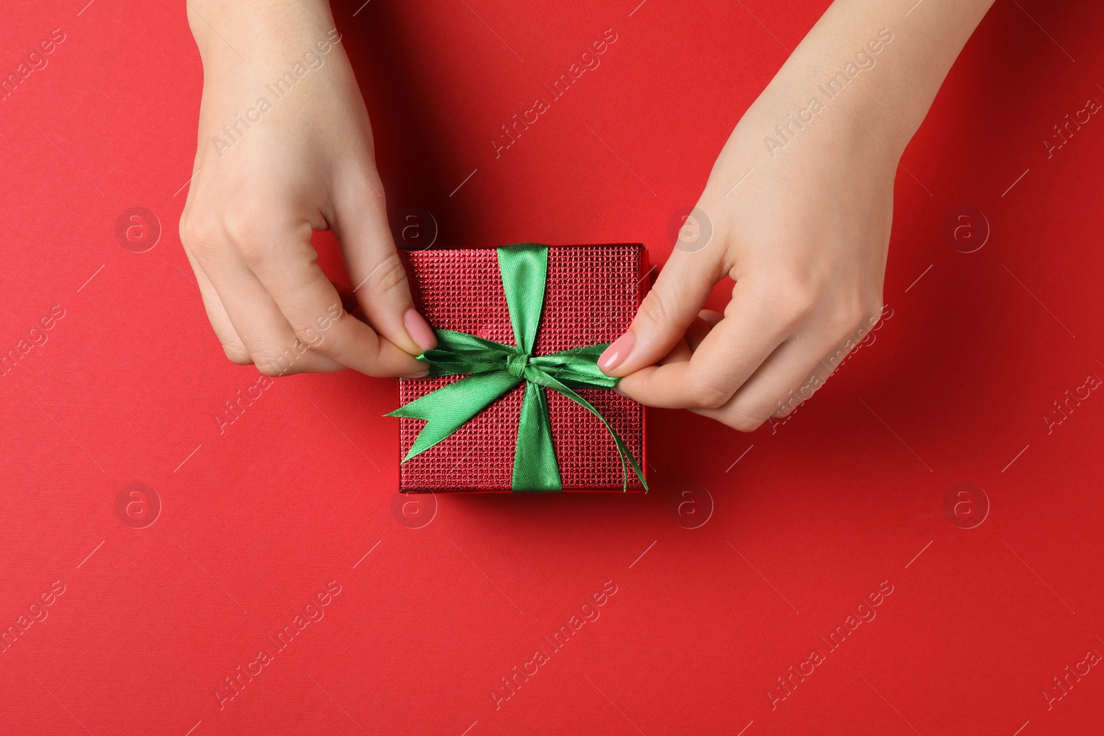 Photo of Woman decorating gift box on red background, top view. Christmas present