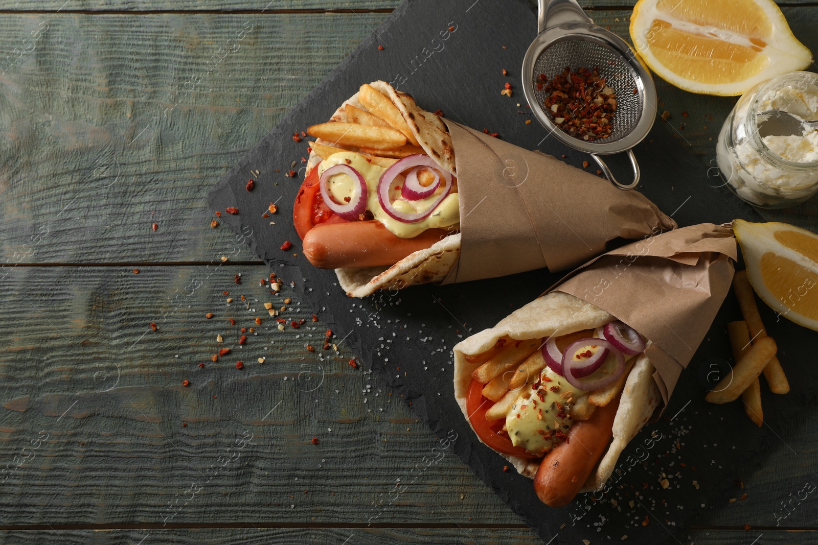 Photo of Delicious pita wrap with sausages, vegetables and potato fries on dark wooden table, top view. Space for text