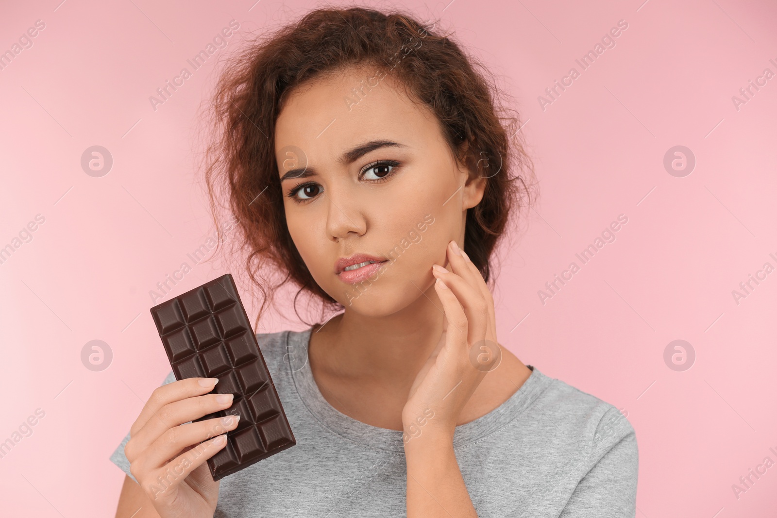 Photo of Beautiful young woman with acne problem holding chocolate on color background. Skin allergy