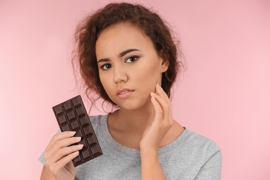 Beautiful young woman with acne problem holding chocolate on color background. Skin allergy