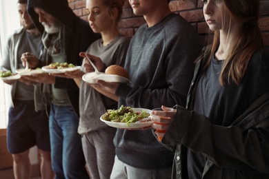 Poor people with plates of food at wall indoors