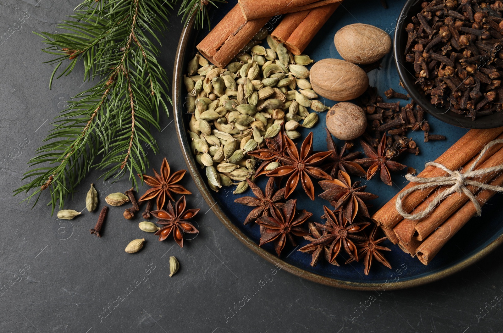 Photo of Dishware with different spices, nuts and fir branches on gray table, flat lay