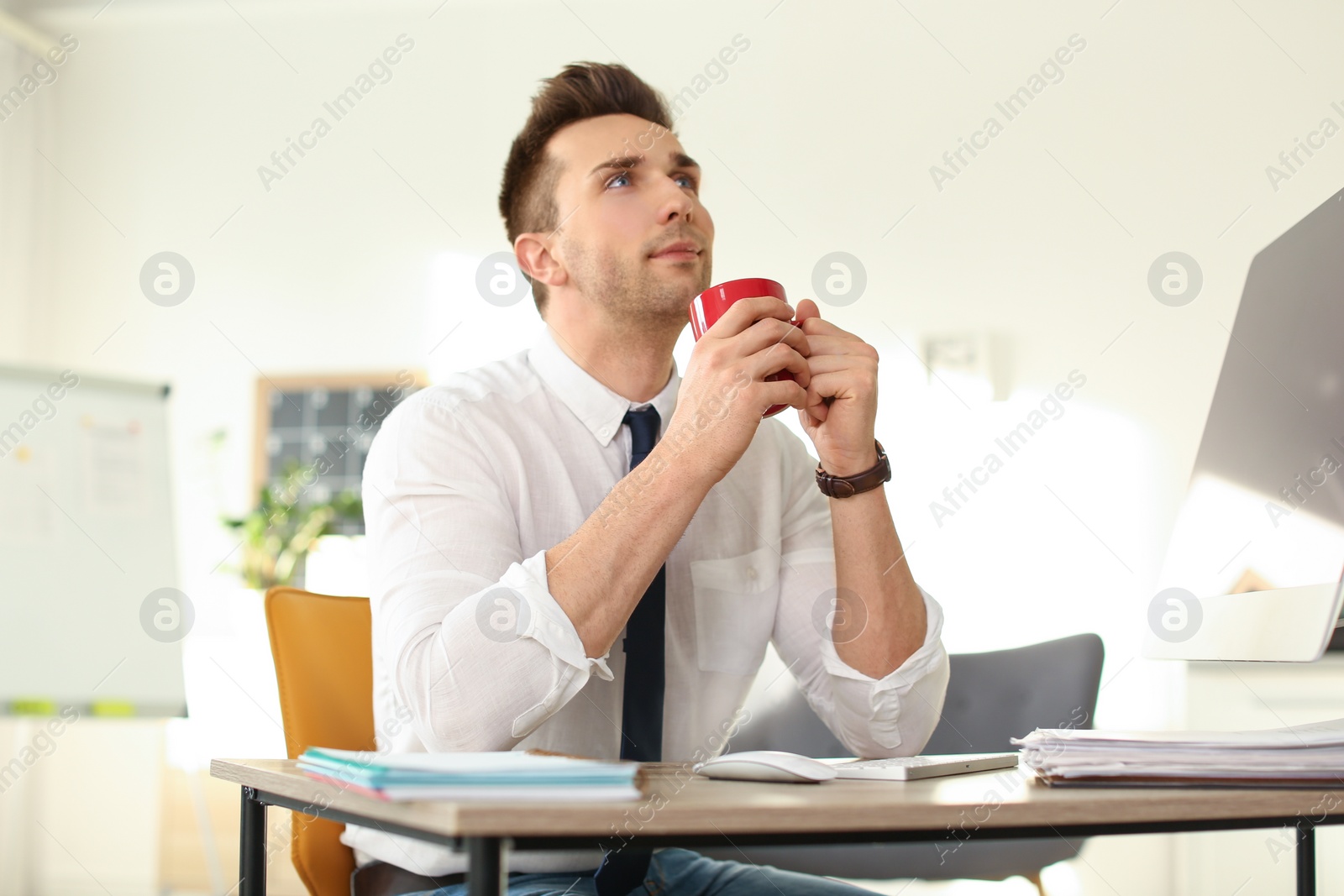 Photo of Young businessman with cup of drink relaxing at table in office during break