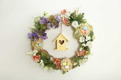Photo of Beautiful decorative wreath with wooden house hanging on white wall. Easter photo zone