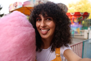 Funny woman with cotton candy taking selfie at funfair