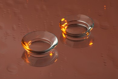 Photo of Pair of contact lenses on wet brown reflective surface