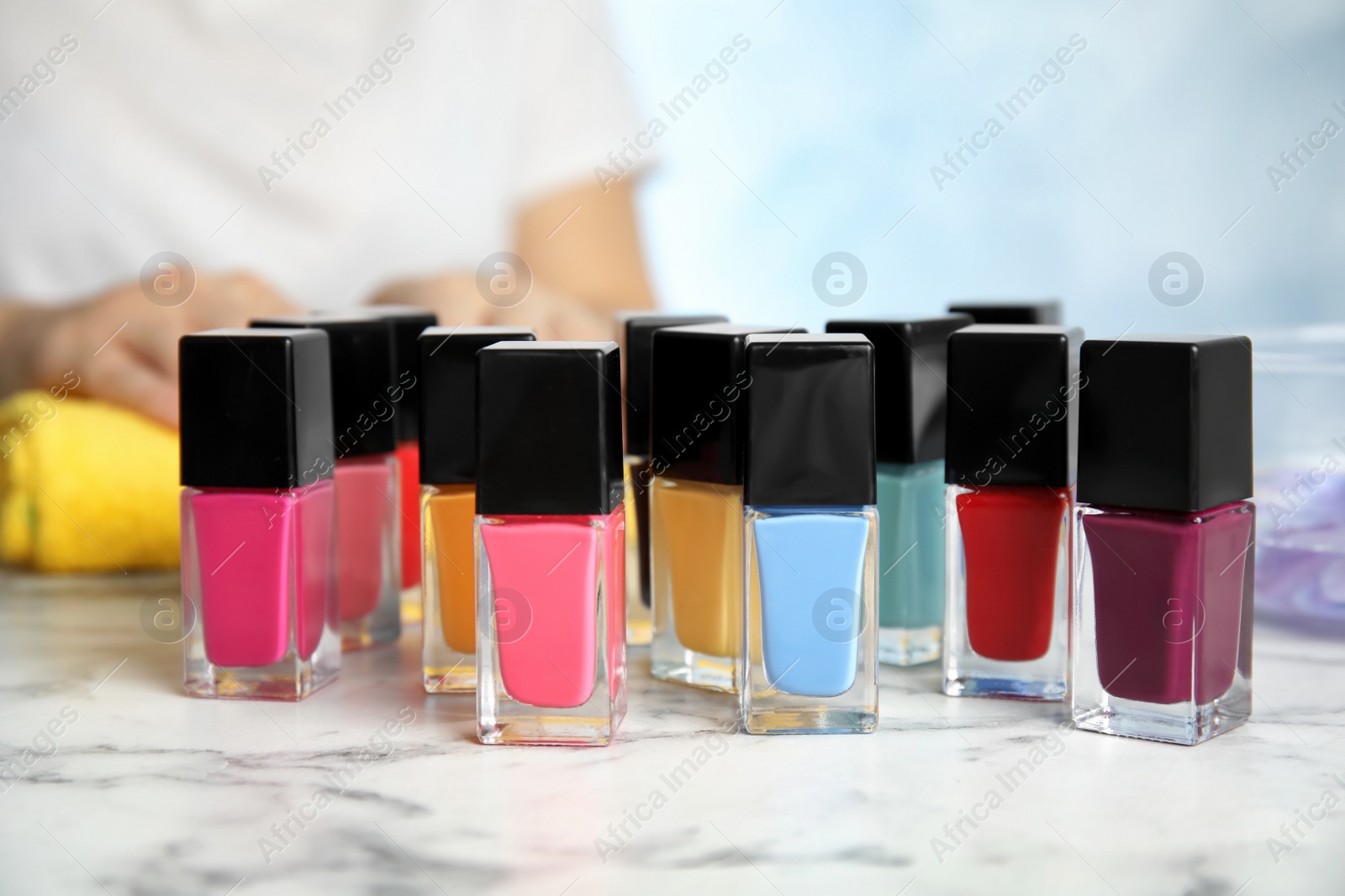 Photo of Bottles of bright nail polish and blurred woman on background