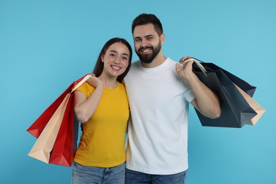 Happy couple with shopping bags on light blue background