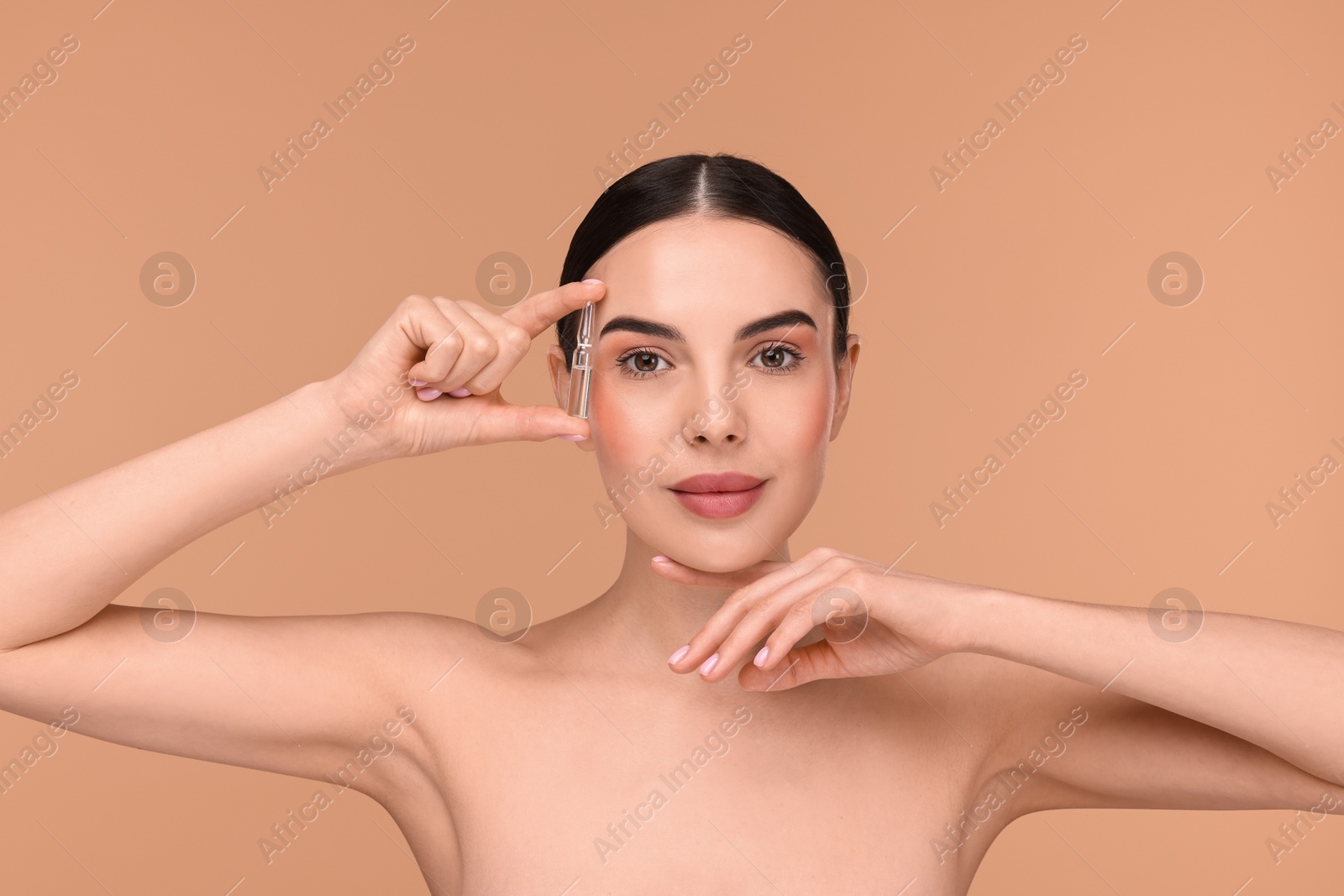 Photo of Beautiful young woman holding skincare ampoule on beige background