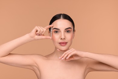 Beautiful young woman holding skincare ampoule on beige background