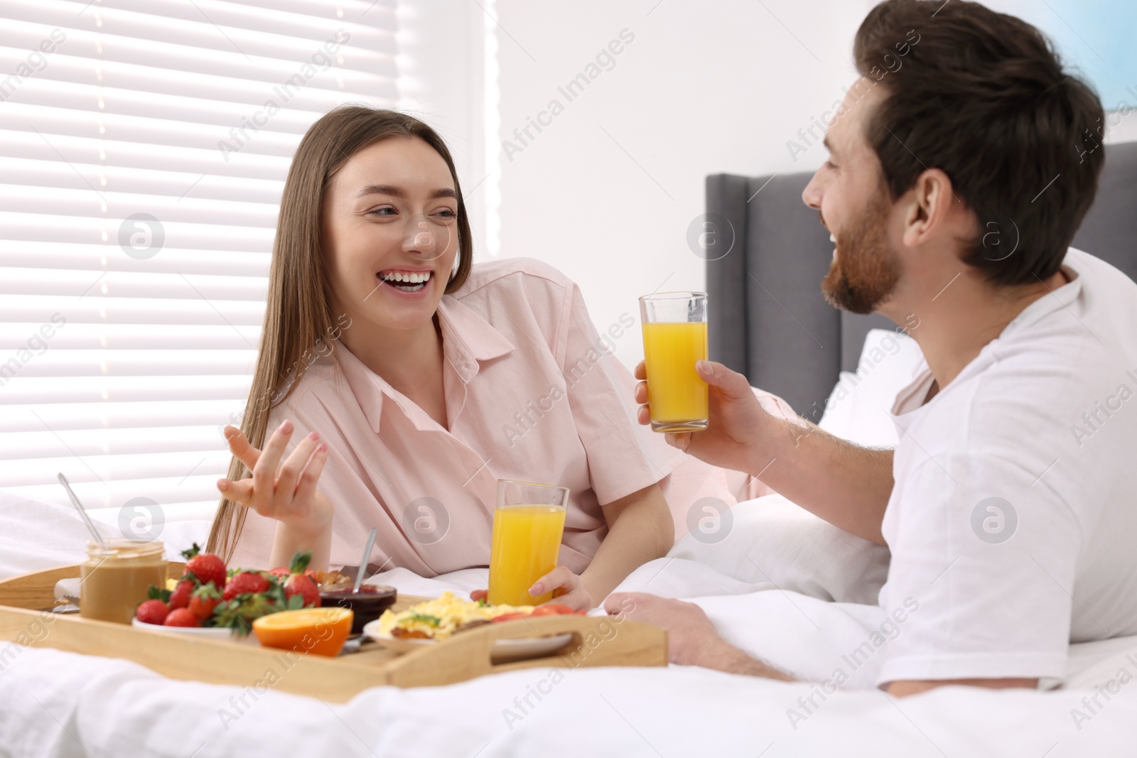 Photo of Happy couple having breakfast and talking on bed at home