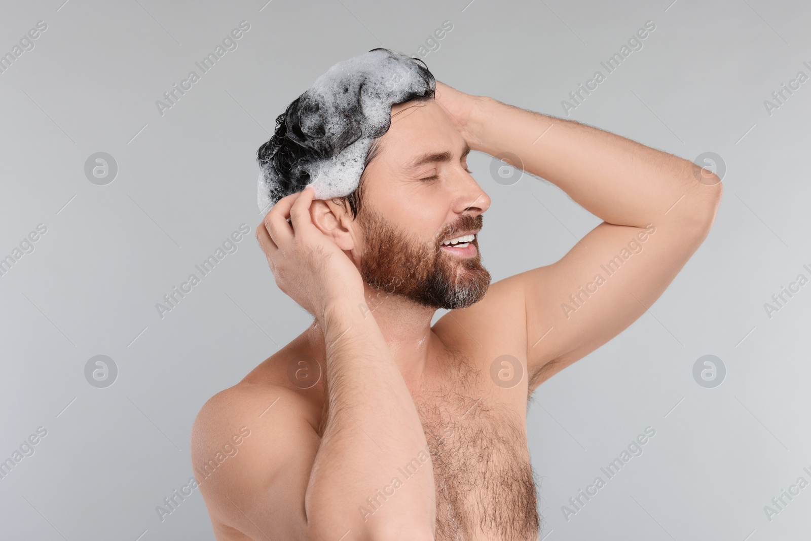 Photo of Happy man washing his hair with shampoo on grey background