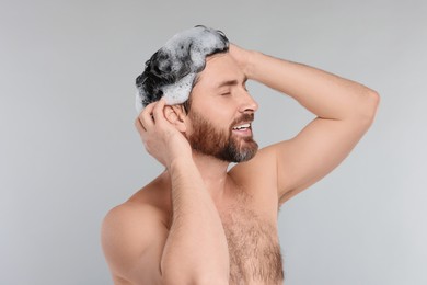 Photo of Happy man washing his hair with shampoo on grey background